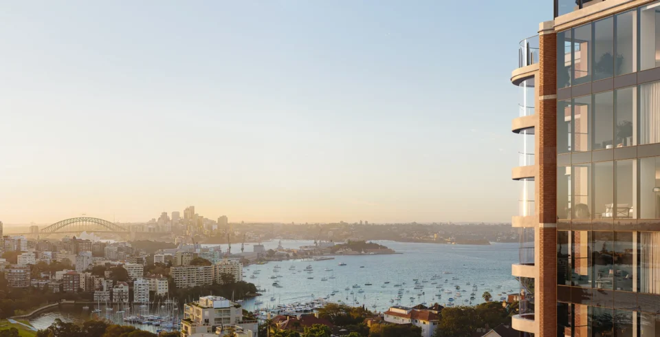 Elevated panoramic view of Sydney Harbour at sunset, featuring a modern glass building in the foreground and the Harbour Bridge in the distance.
