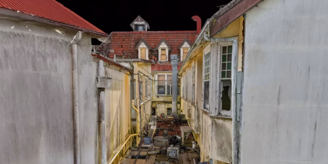 A detailed 3D photogrammetry model of a narrow alleyway within an abandoned complex, showing weathered white walls, broken windows, and debris-cluttered roofs against a black background.