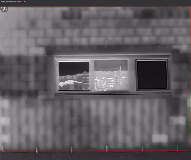 Grayscale thermal drone image of a building facade revealing moisture ingress and cool spots below a window.