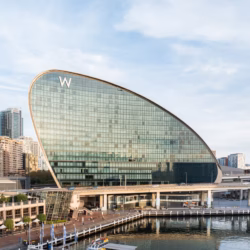 The W Sydney hotel's distinctive curved glass building overlooking Darling Harbour, featuring a prominent "W" logo and modern architecture.
